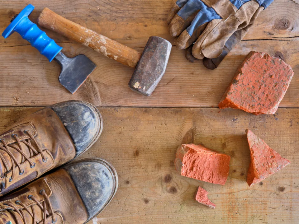 Work boots, hammer, chisel and broken bricks on a wooden surface